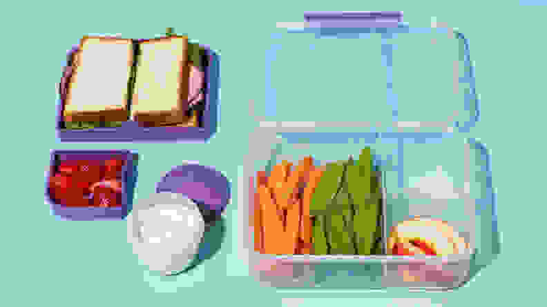 A clear plastic Bento box filled with vegetables, fruit, and a sandwich.