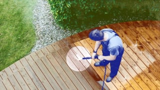 Person using power washer on wooden deck outdoors to clean boards.