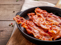 Strips of bacon in a skillet on a wooden board
