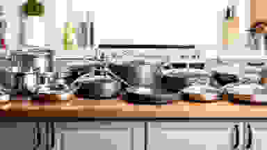 Three complete cookware sets are lined up on a kitchen island