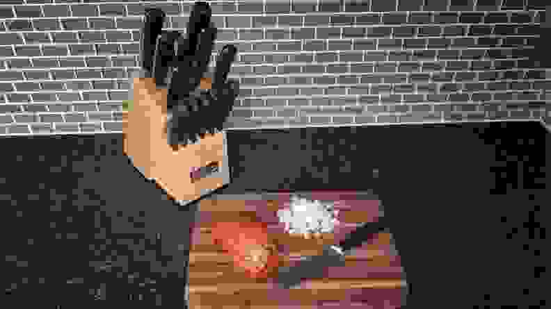 Cuisinart knife block set next to a cutting board with sliced onions and tomatoes on a countertop.