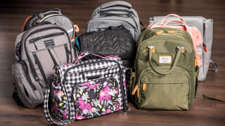 Nine diaper bags arranged in a group on a hardwood floor