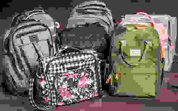 Nine diaper bags arranged in a group on a hardwood floor