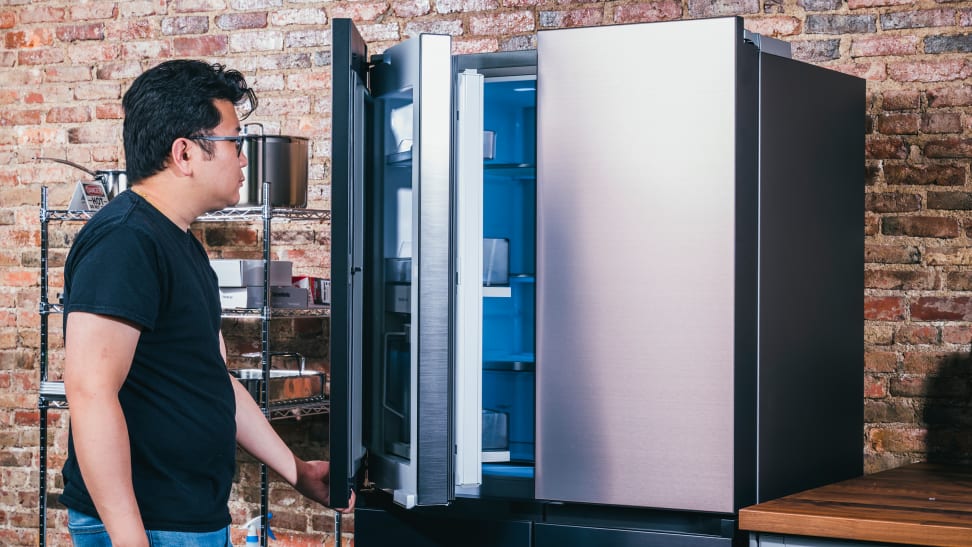 An Asian man opens a door to a stainless steel refrigerator