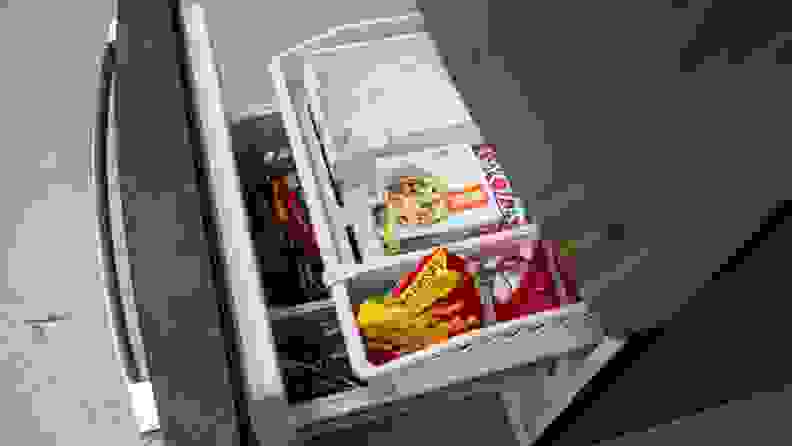 Bottom freezer drawer pulled out to display the ice tray and two-level drawers filled with assorted frozen food packages.