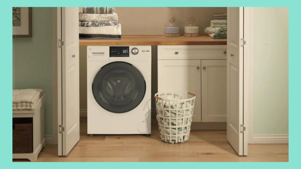 A GE washer-dryer combo is nestled in a small laundry closet with a basket of clothes beside it.