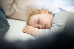 A blonde toddler sleeping in a bed with a pillow.