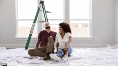 A couple sitting on the floor of an empty house with tarps on the floor.