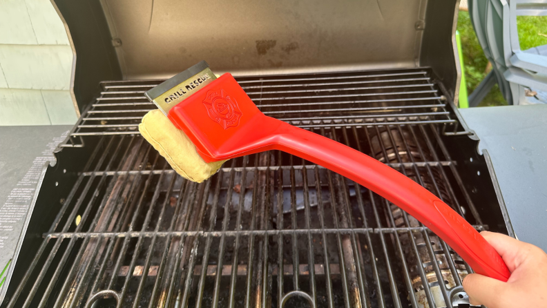 A Grill Rescue brush being held over an open grill.