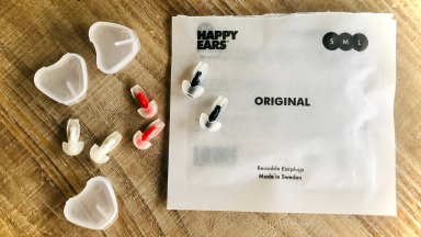 Red, white, and black earplugs sit next to three heart-shaped cases and a white square bag on a brown wooden countertop