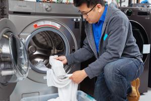 An Asian man pulls white socks and towels out of a washing machine