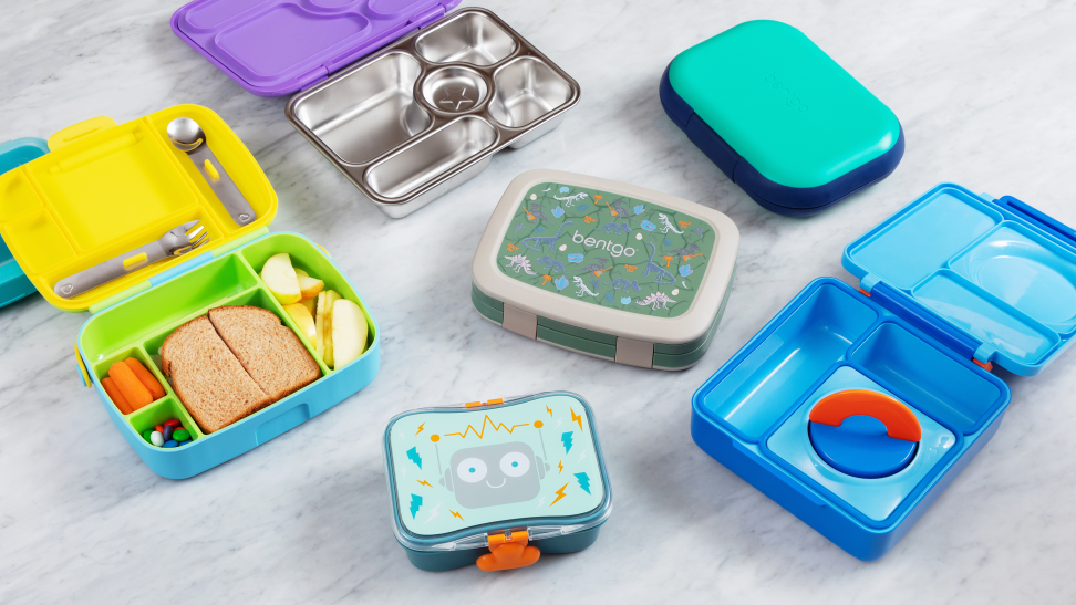 A variety of brightly colored lunch boxes sit open and closed on a marble counter.