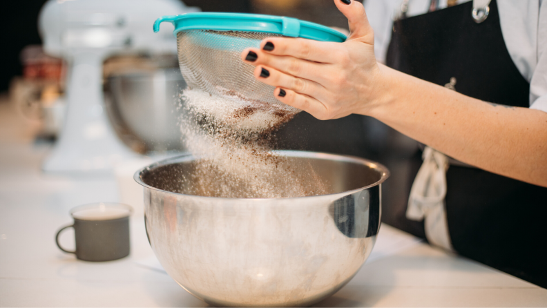 A hand sifting flour into a mixing bowl