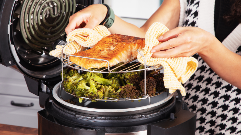 A person lifts a tiered metal rack loaded with cooked food out of a Ninja Foodi.