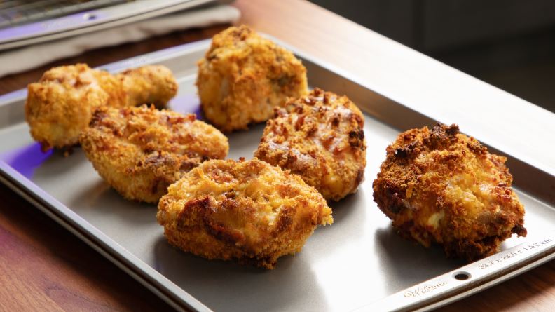 Six pieces of frozen chicken cooked on a cookie sheet after exiting a Ninja Foodi air fryer.