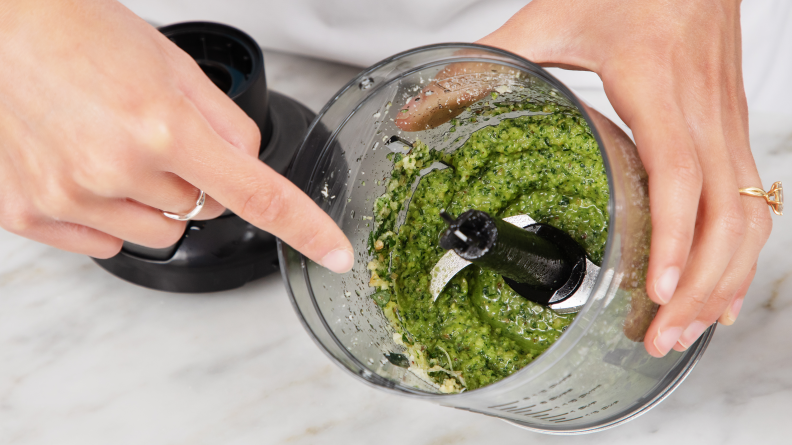 A person pointing at the inside of the Black & Decker Kitchen Wand mixing bowl accessory, with pesto inside the bowl.