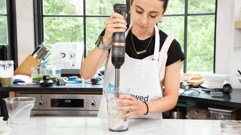 A person holding the Black & Deck Kitchen Wand and mixing liquid inside a container.