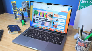 A new Apple laptop flipped open and turned on, sitting on top of a desk with several objects