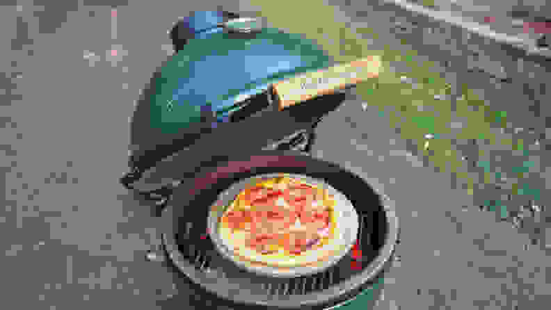 A Big Green Egg, opened, revealing a pepperoni pizza as it cooks.