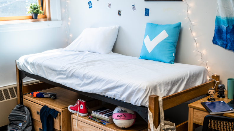 A twin bed in a college dorm surrounded by shoes, clothes, decorations, and school supplies.