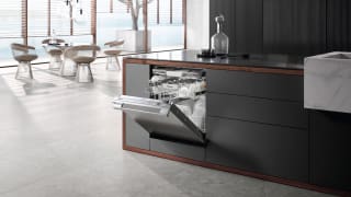 An image of a modern kitchen that includes the Miele dishwasher. Its door is open, revealing its inner racks stocked with spotless dishes.