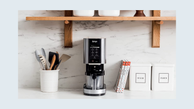 Ninja Creami on a white counter in a kitchen under a wood shelf.