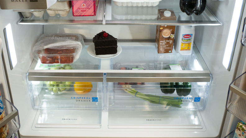 The lower, interior portion of a fridge with crisper drawers filled with grapefruit and green onions