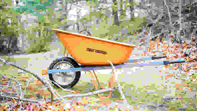 An orange True Temper wheelbarrow sits in a wooded area.