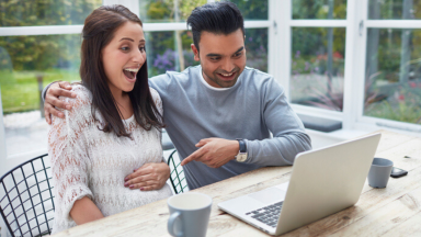 A pregnant woman and man sitting at an outdoor patio table using the computre