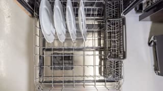 The lower rack of a dishwasher is filled with four white plates