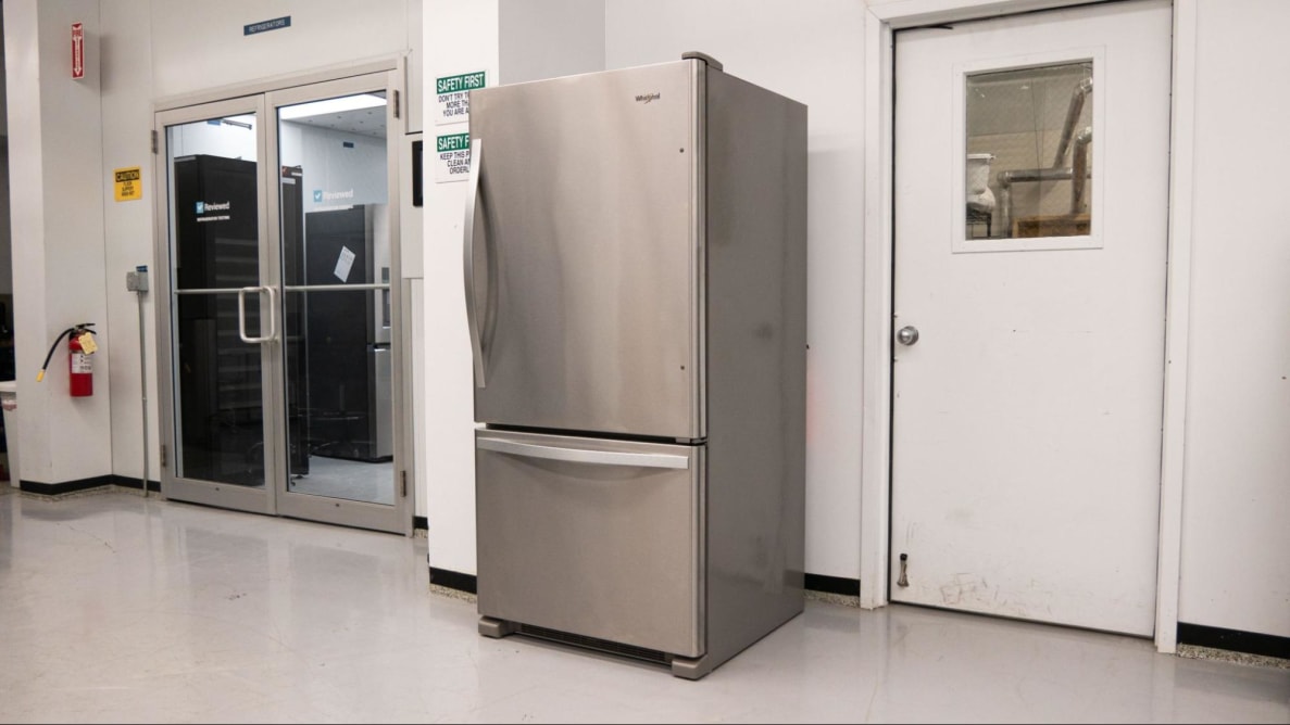 A stainless steel refrigerator sits against a white wall in a laboratory environment.
