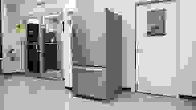 A stainless steel refrigerator sits against a white wall in a laboratory environment.