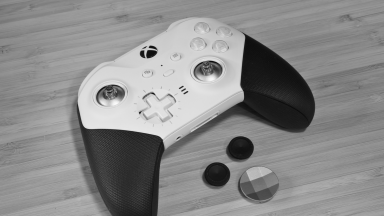 Close-up of an Xbox wireless controller, white with black rubber grips, on a wood-grain surface. The thumbstick grips and smooth chrome D-pad button have been removed for display.