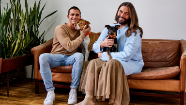 Antoni Porowski and Jonathan Van Ness sitting with their dogs on a couch.